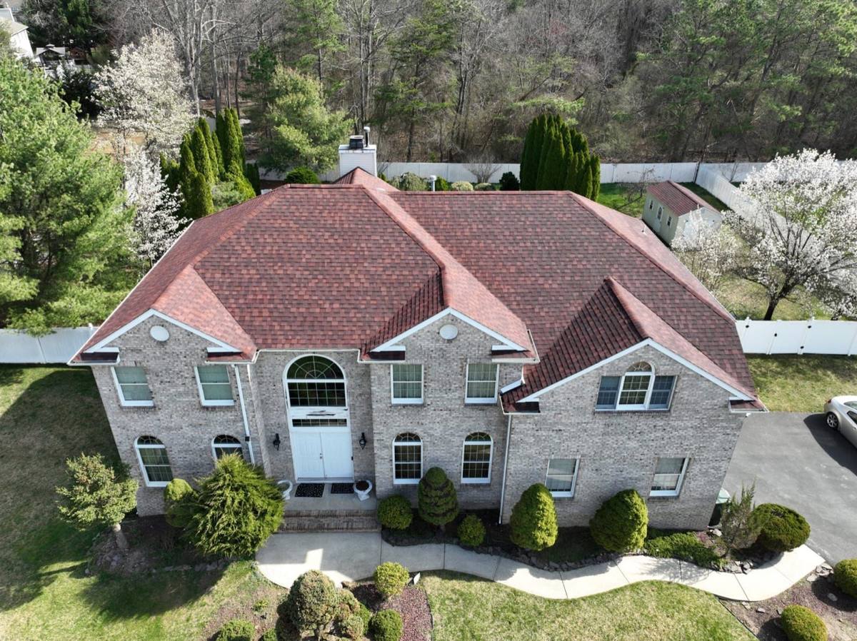 Aerial drone shot of a completed brick mansion with deep burgundy shingles